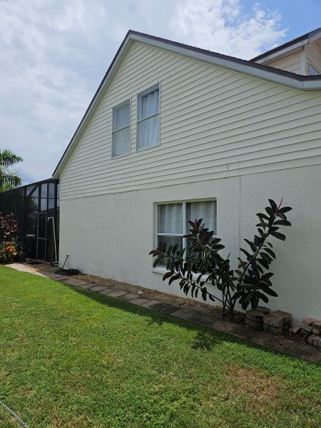 A two-story house with cream siding and stucco exterior, featuring two top windows, one lower window, and a dark bush.