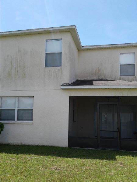Two-story beige apartment building with a dark screened entrance and small grass yard