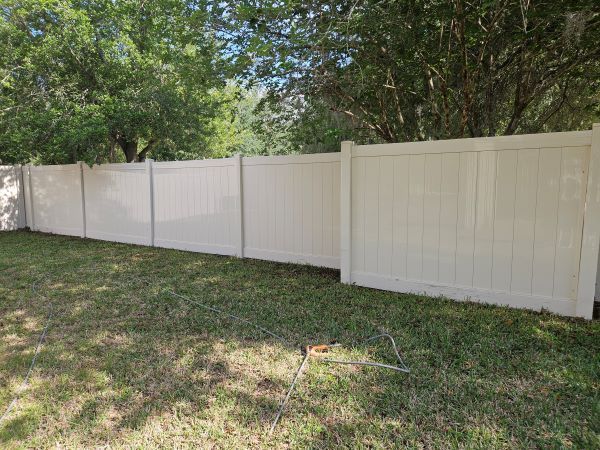 Green screened-in patio/courtyard beside a hedge and wet lawn, with potted plants and a stone path.
