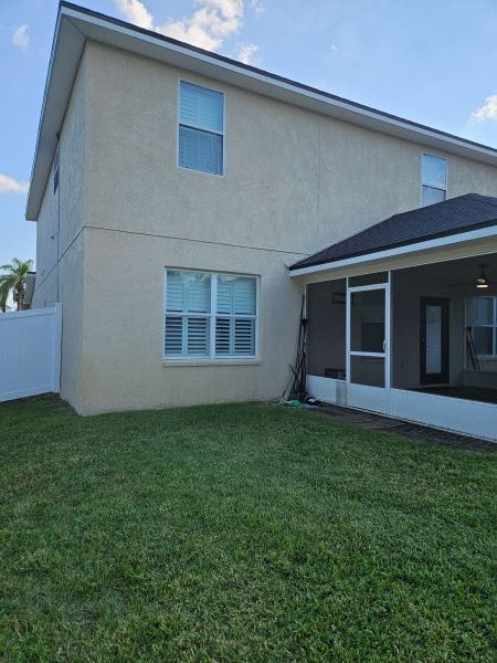 Green screened-in patio/courtyard beside a hedge and wet lawn, with potted plants and a stone path.