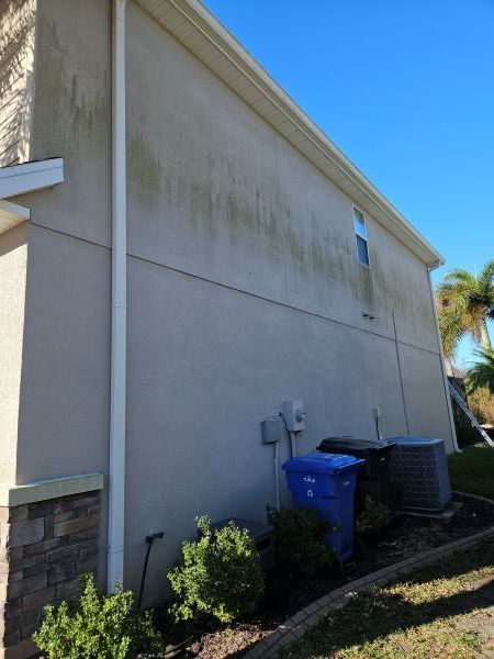 A tan stucco exterior wall under a white roof eave against a vibrant blue sky with fluffy white clouds.