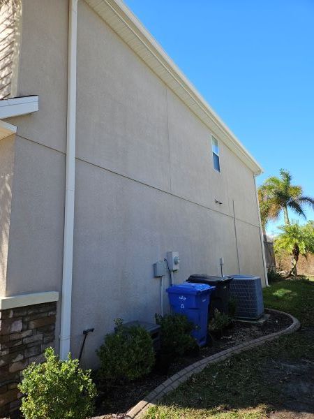 A tan stucco exterior wall under a white roof eave against a vibrant blue sky with fluffy white clouds.