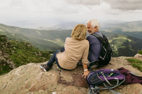 a man and a woman are sitting on top of a rock looking at the mountains .