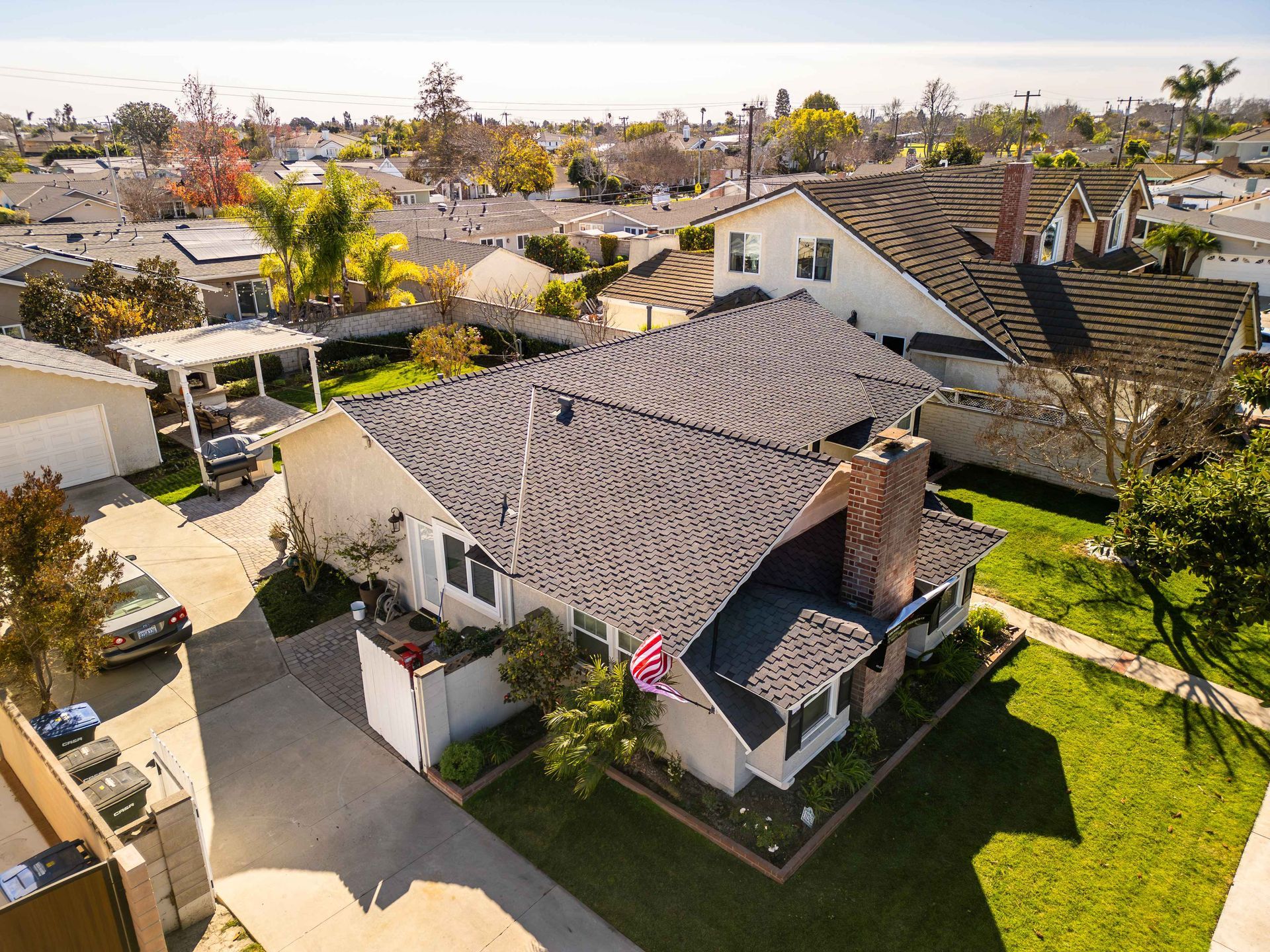Aerial view of a suburban house with a dark gray roof, chimney, and manicured lawn.