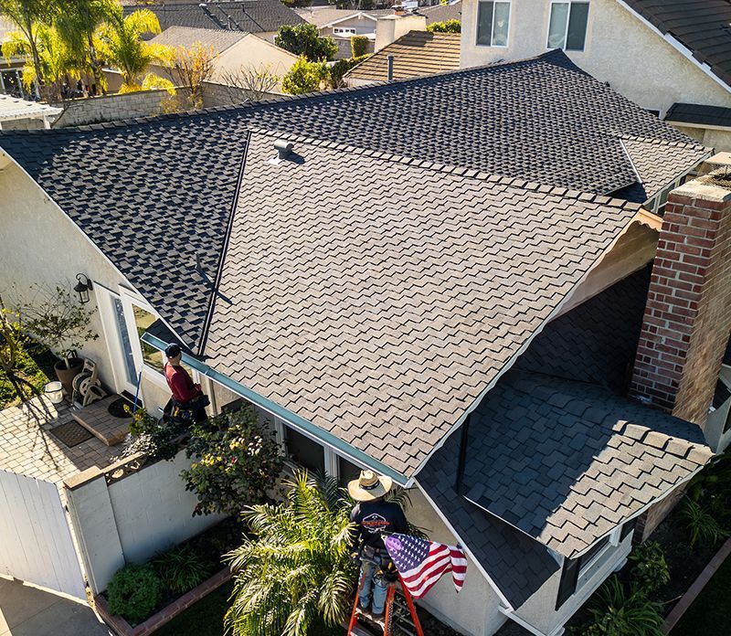 An aerial view of a man on a ladder working on the roof of a house