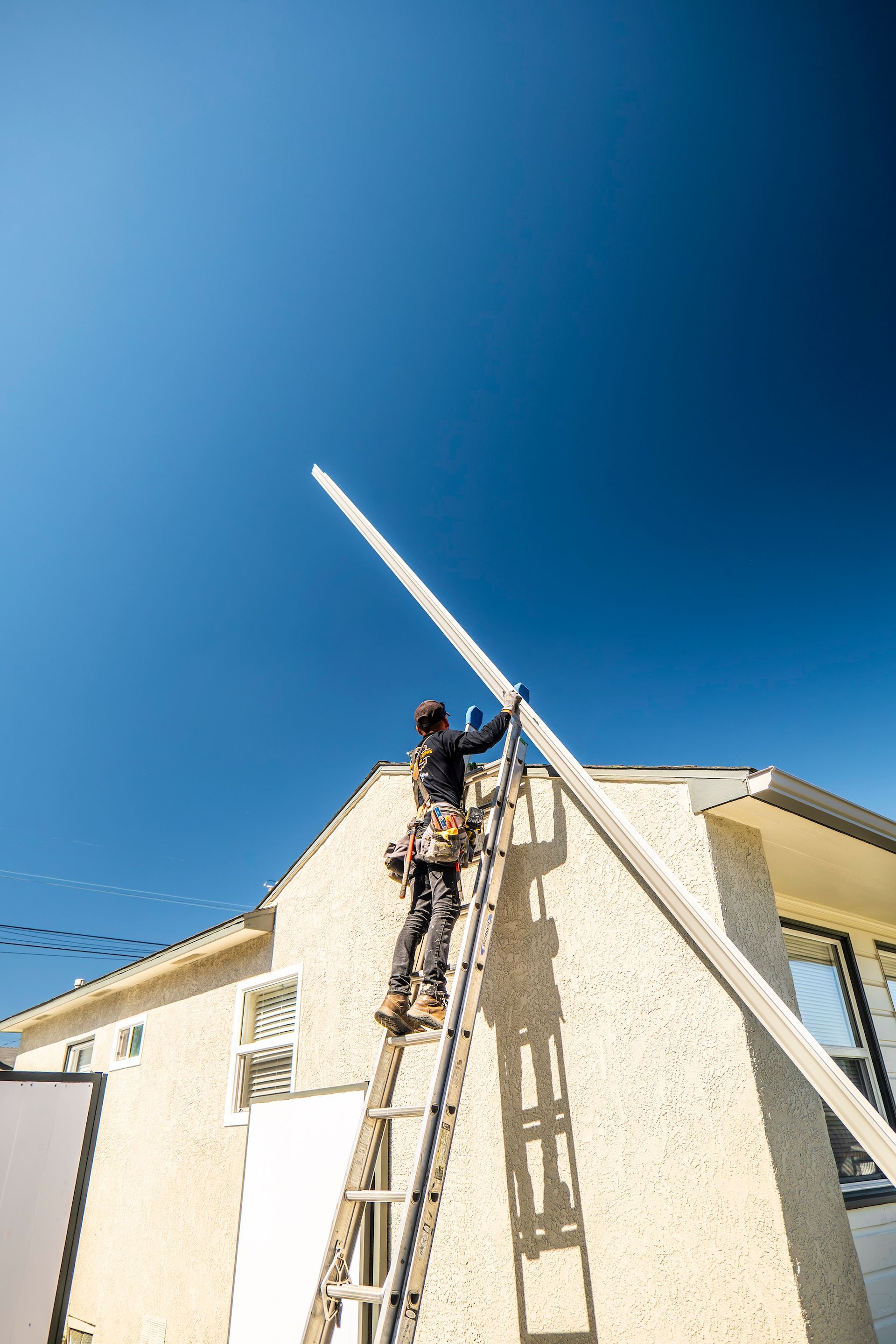 A man is standing on a ladder on the side of a house.