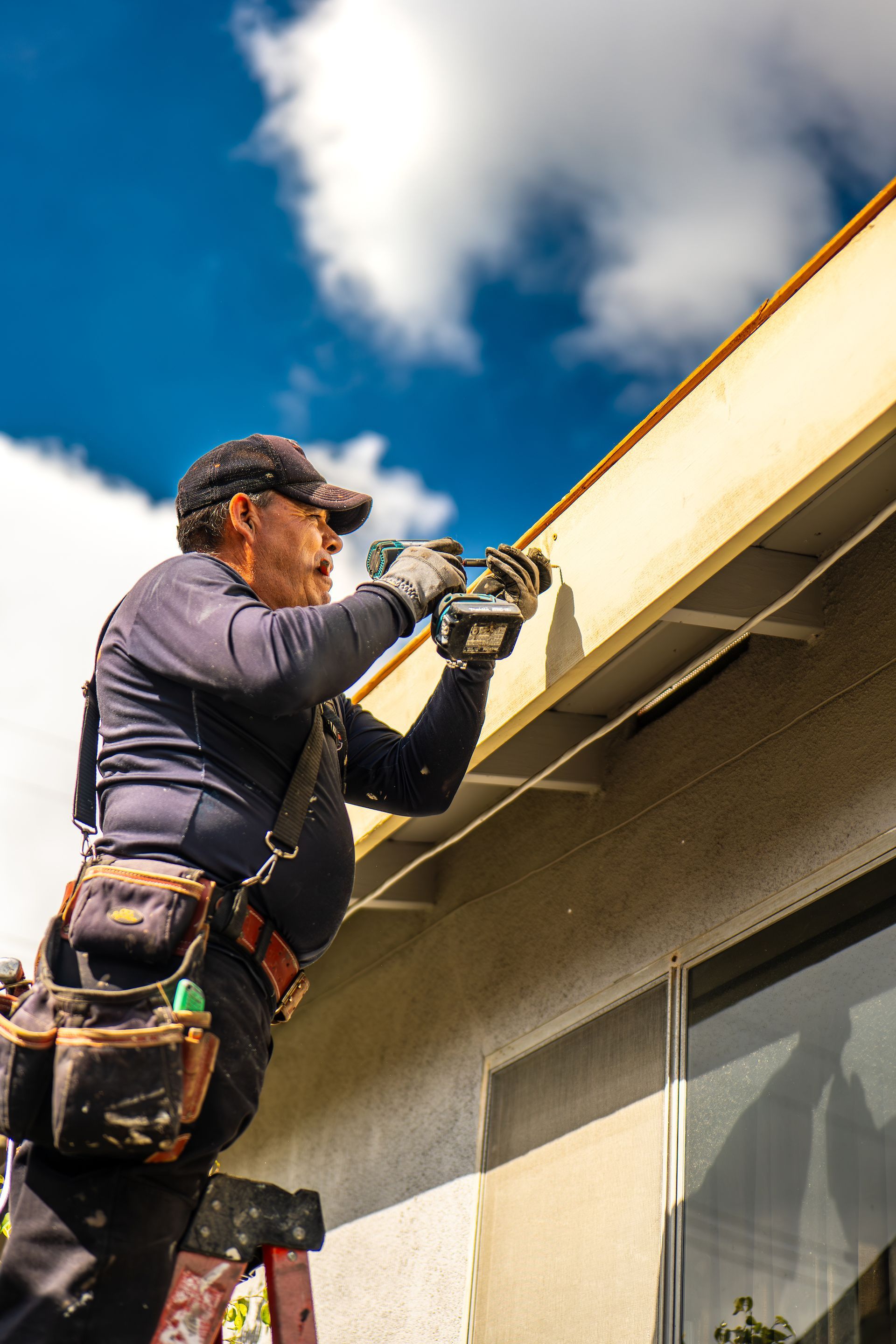 A man is working on the side of a building with a drill.
