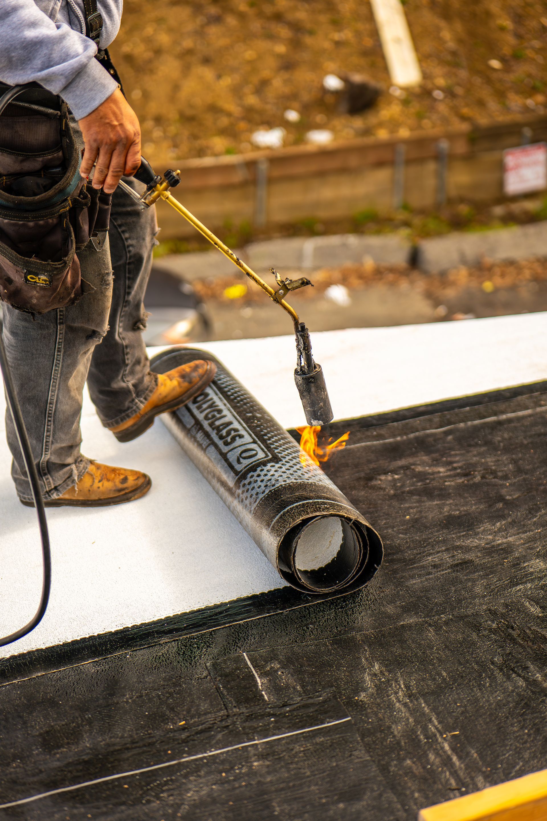 A man is rolling a roll of roofing material on a roof.