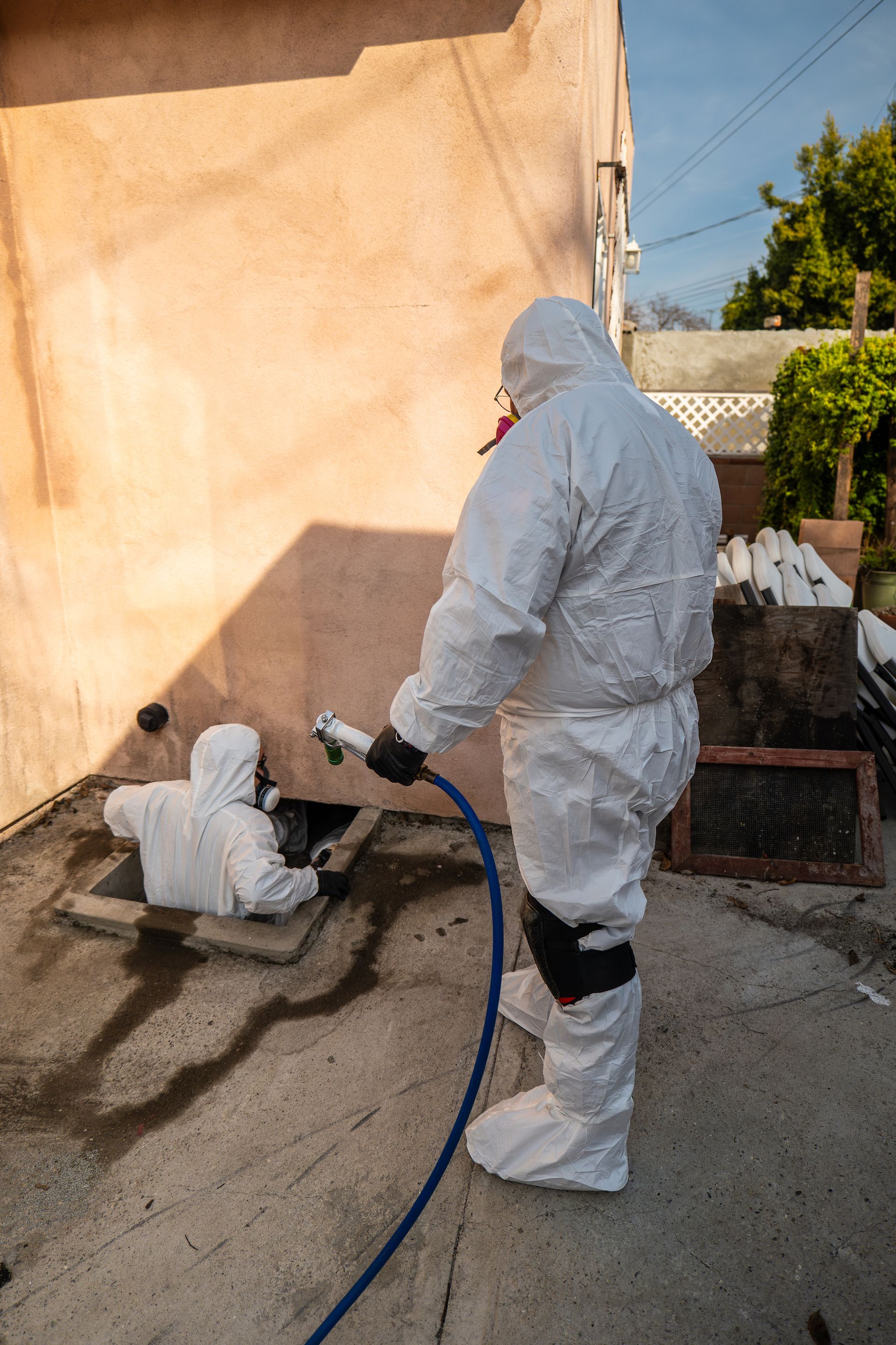 A man in a protective suit is spraying something with a hose.
