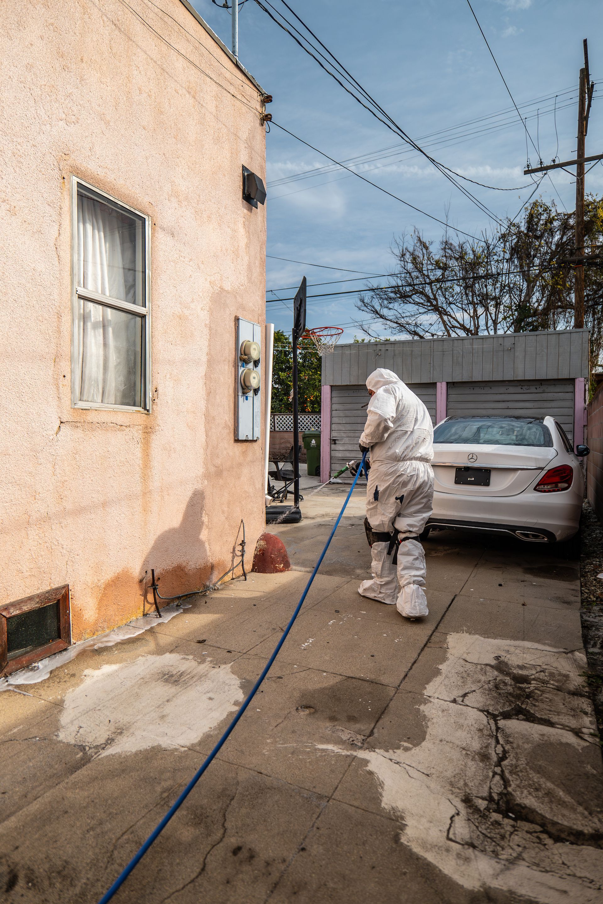 A man in a protective suit is spraying a car with a hose.