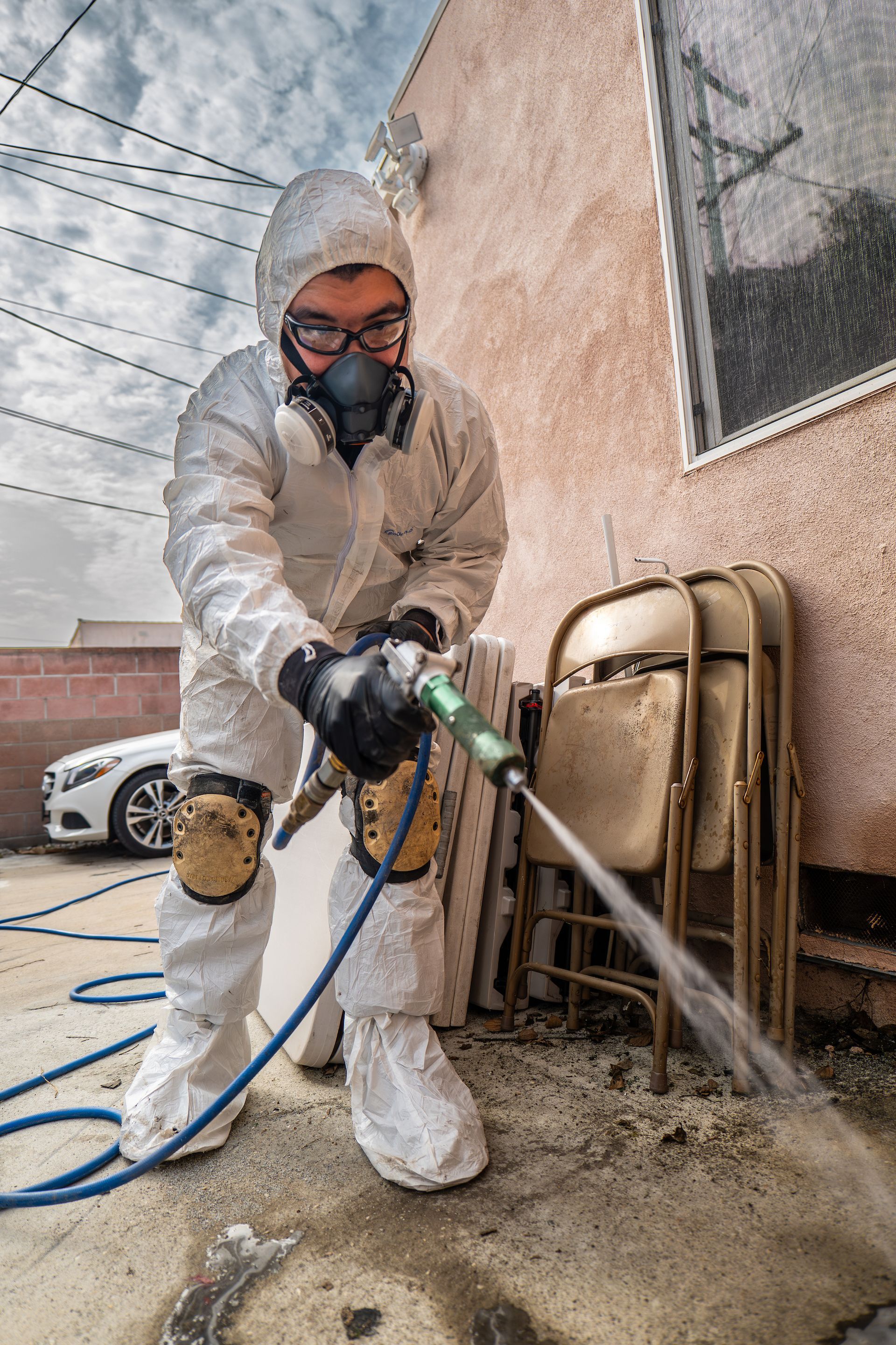 A man in a protective suit is spraying a hose on the ground.