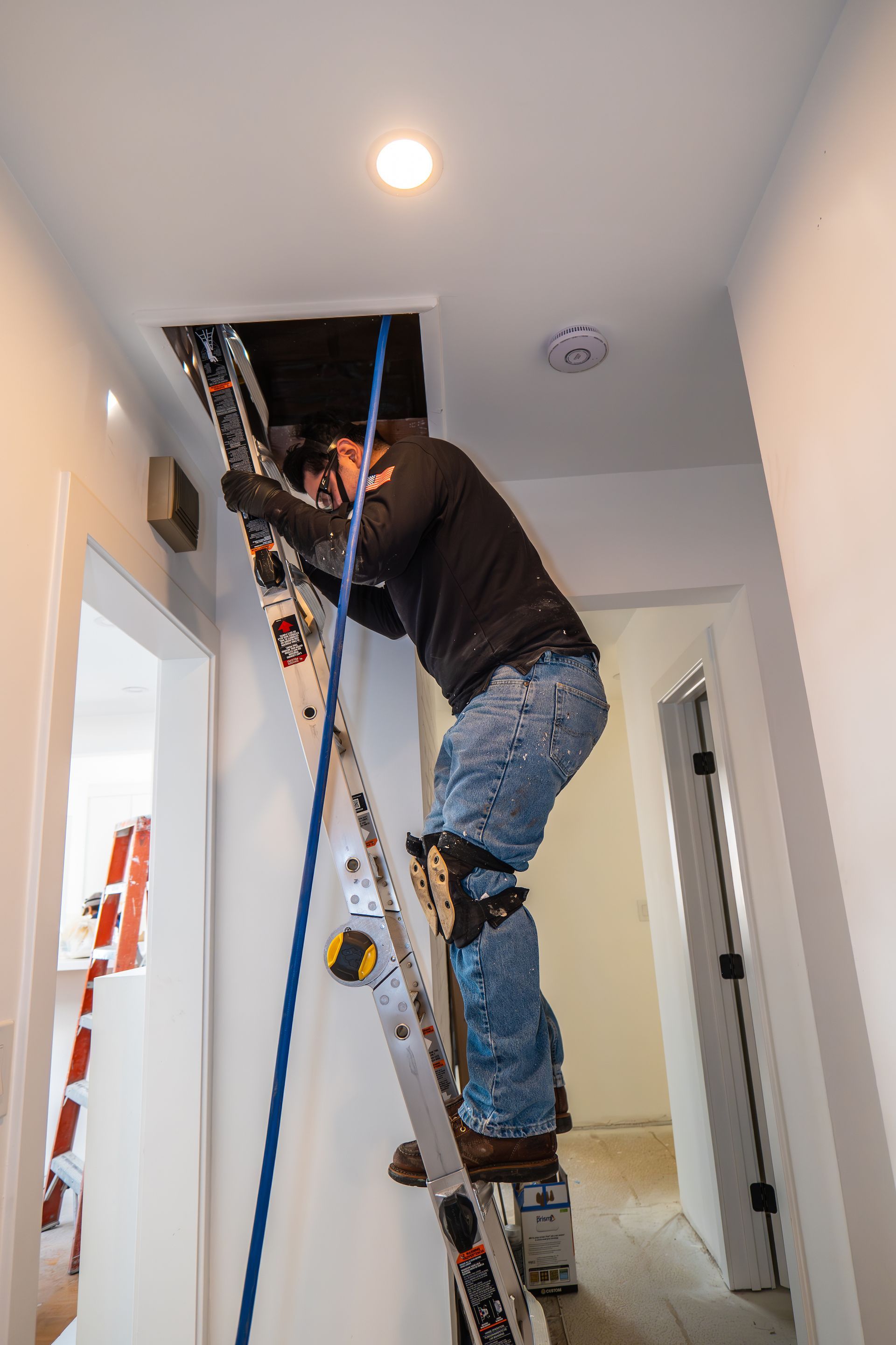A man is climbing up a ladder in a hallway.