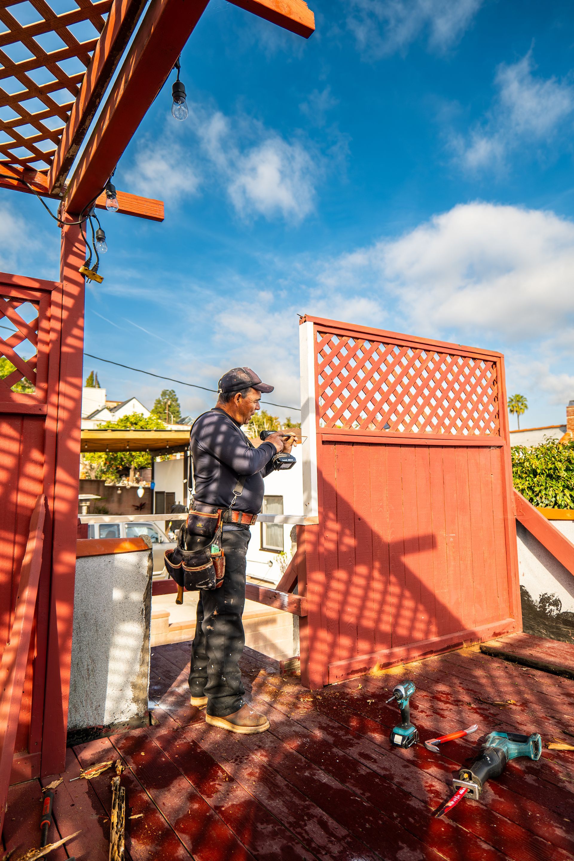 A man is working on a red fence with a drill.