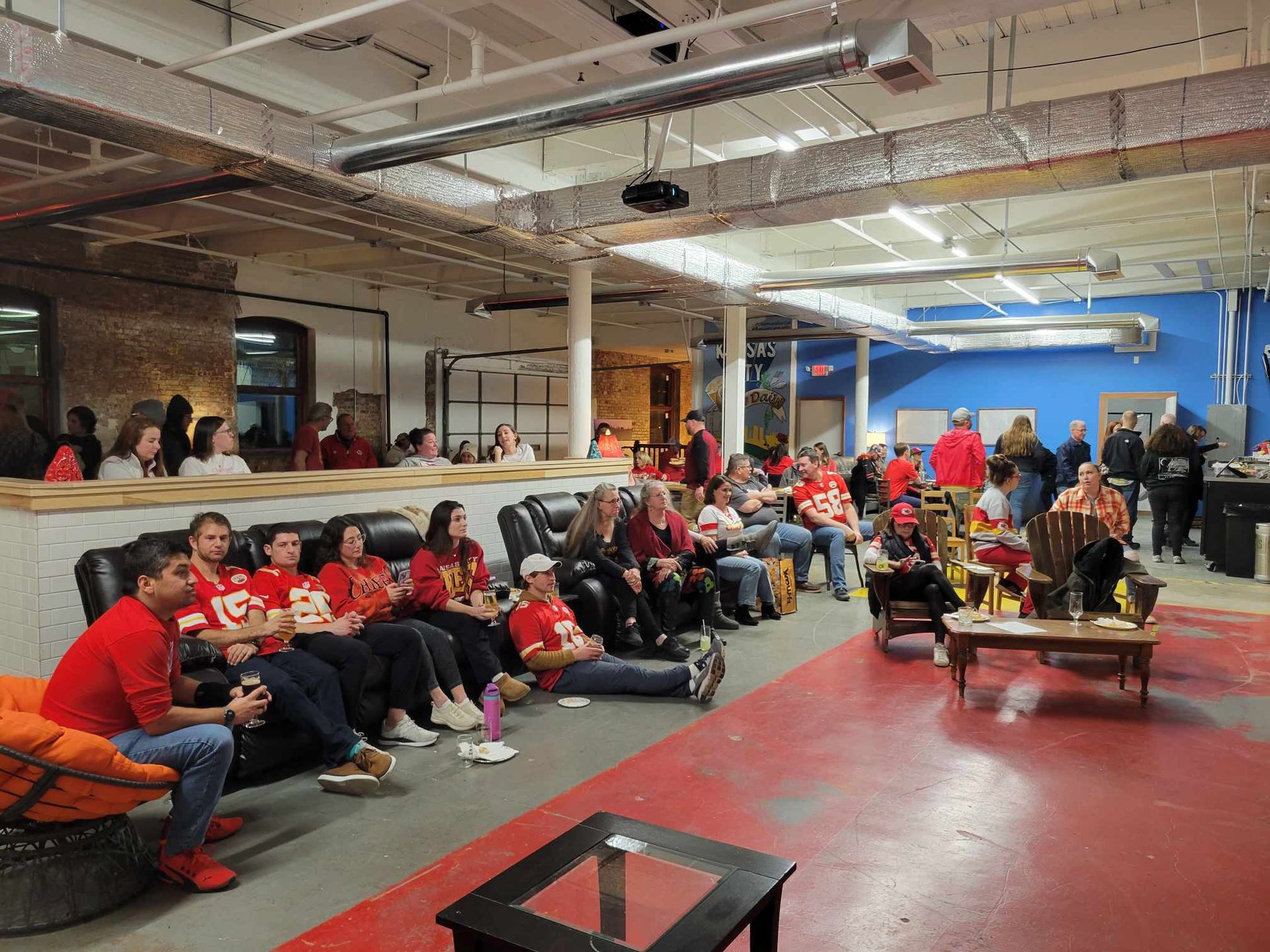 A group of people are sitting in a room watching a local sports event