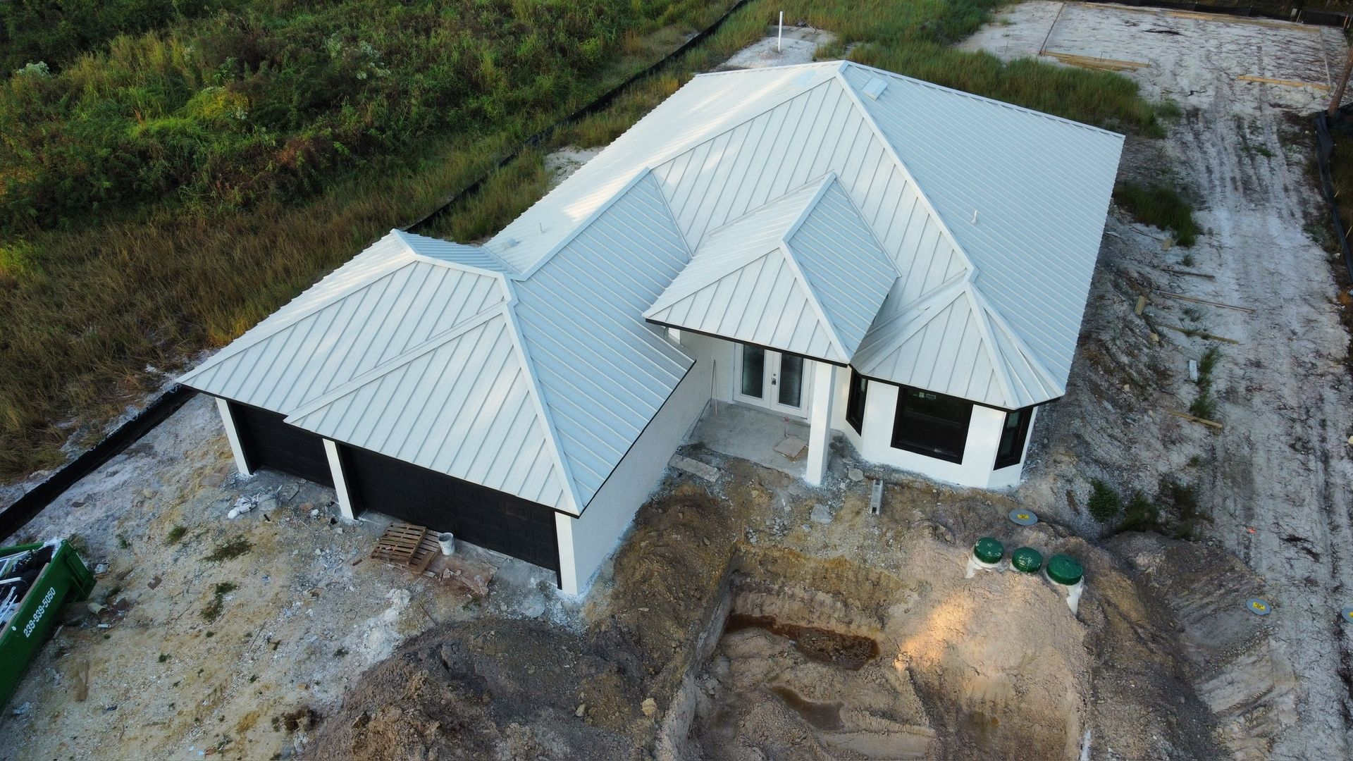 Newly built house with a gray metal roof, black garage doors, and black window frames.
