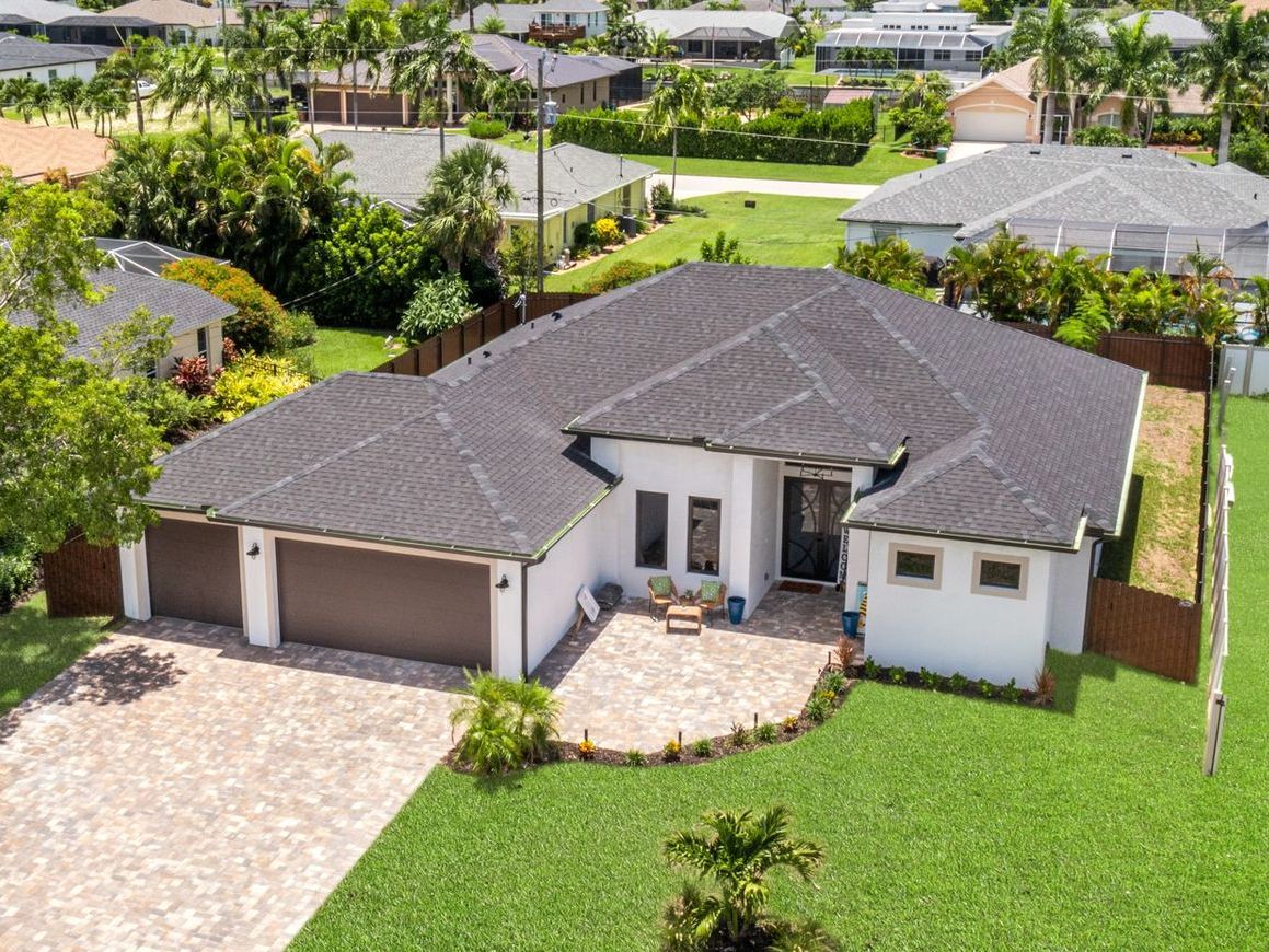 A single-story white house with a brown roof, green lawn, and a paved driveway.