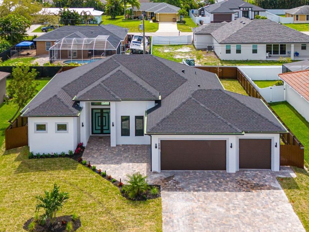 Modern white house with a dark gray roof, brown garage doors, and a brick driveway.
