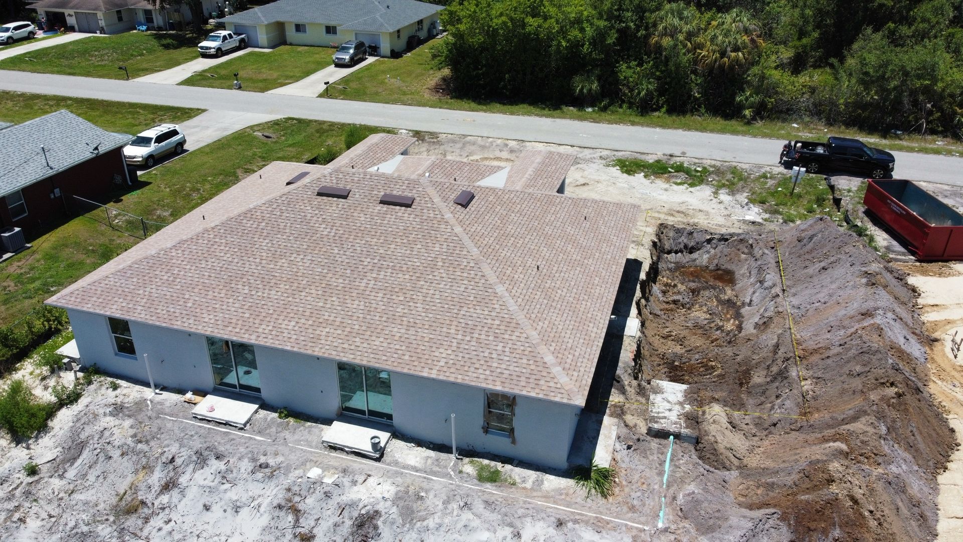 Aerial view of a light blue house with a brown roof under construction, next to a dirt pile.