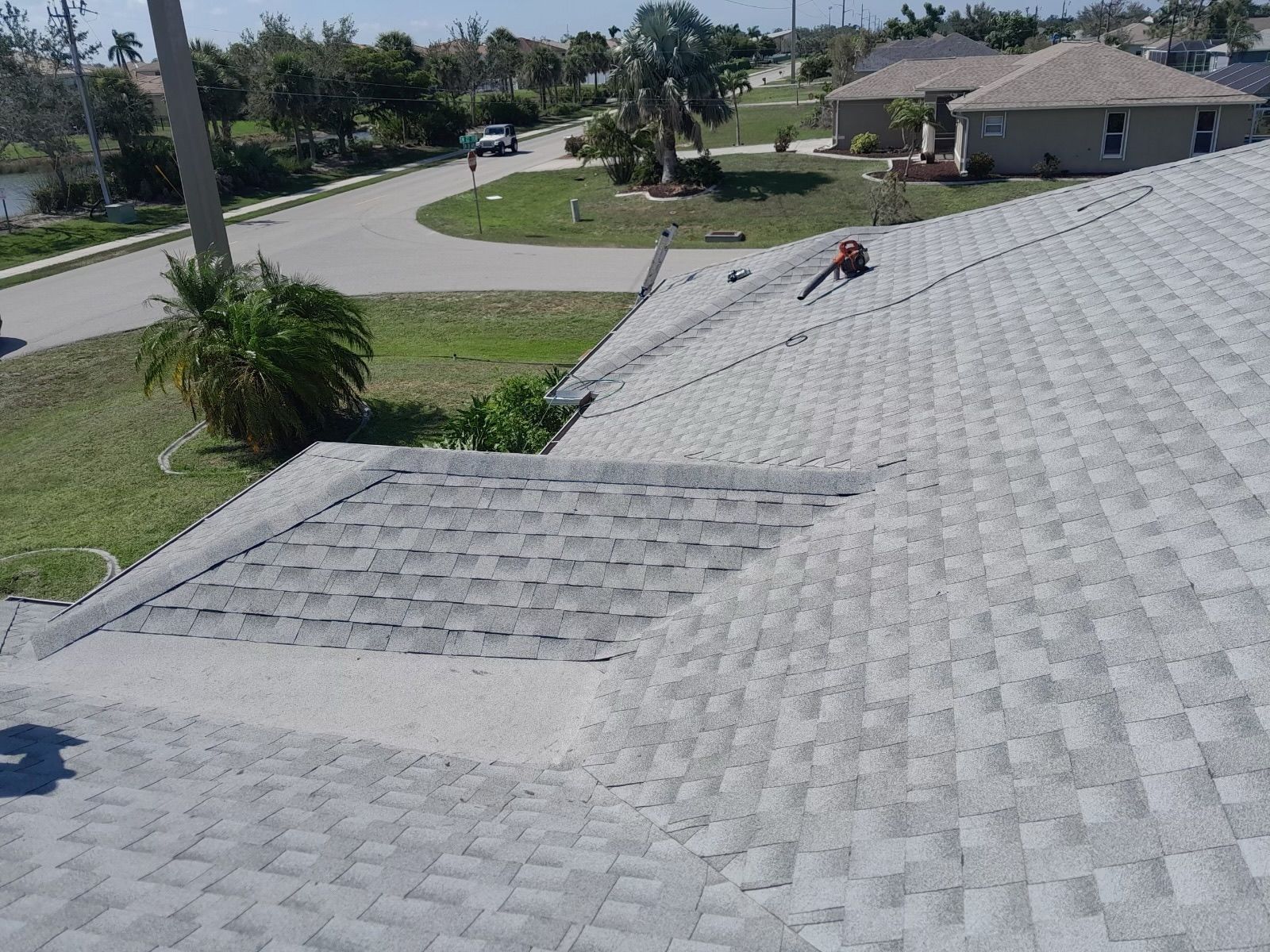 View from a roof: gray shingles, green lawn, palm tree, houses, and a street.