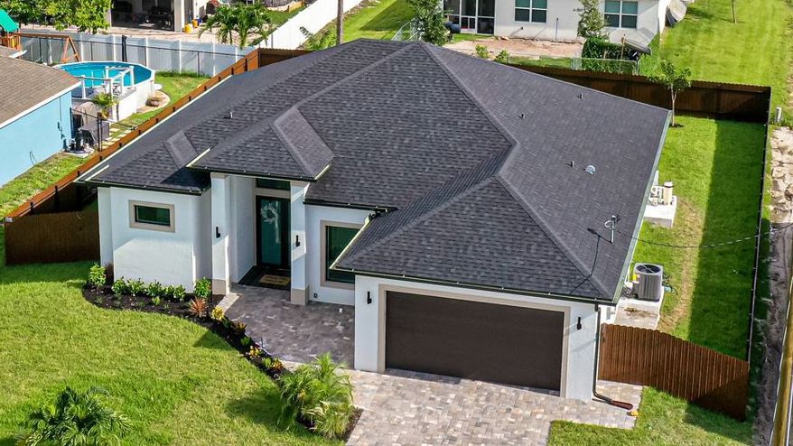 Aerial view of a modern white house with a dark gray roof and a manicured lawn.