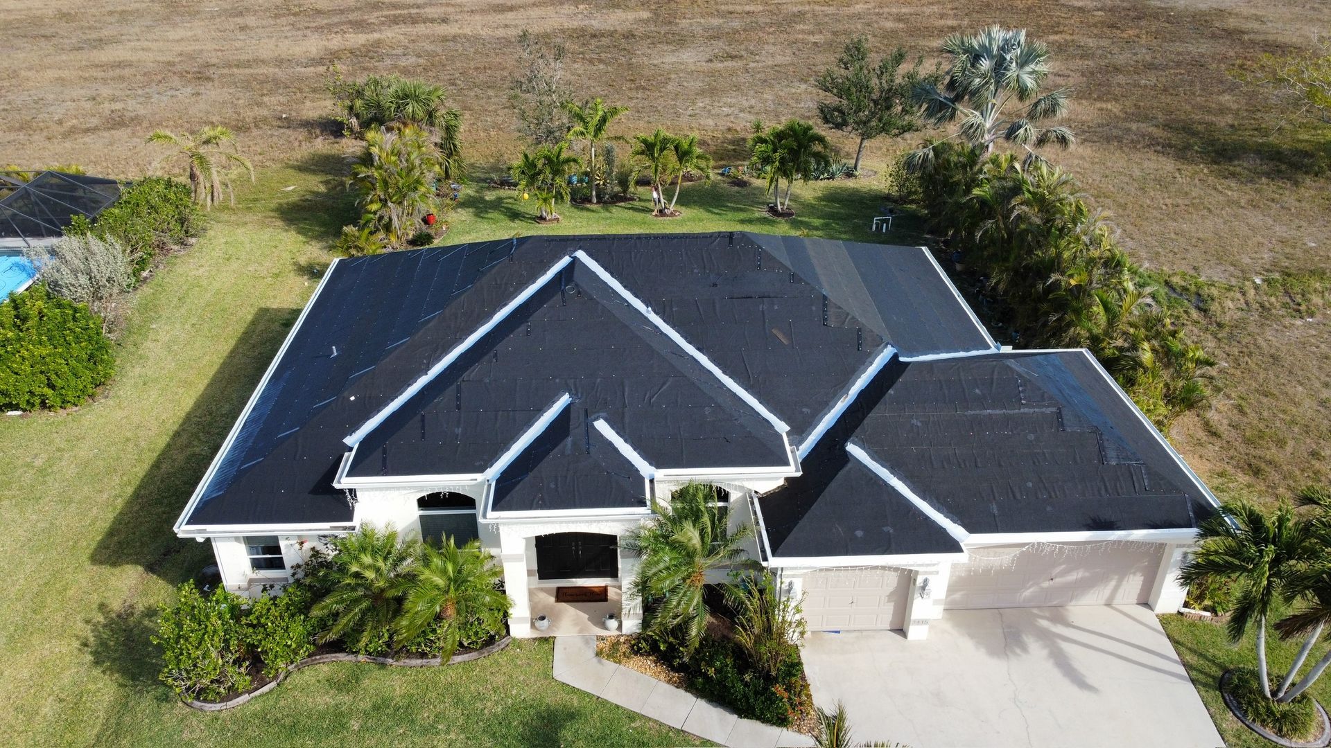 Aerial view of a white house with a dark roof and green landscaping. Driveway visible.