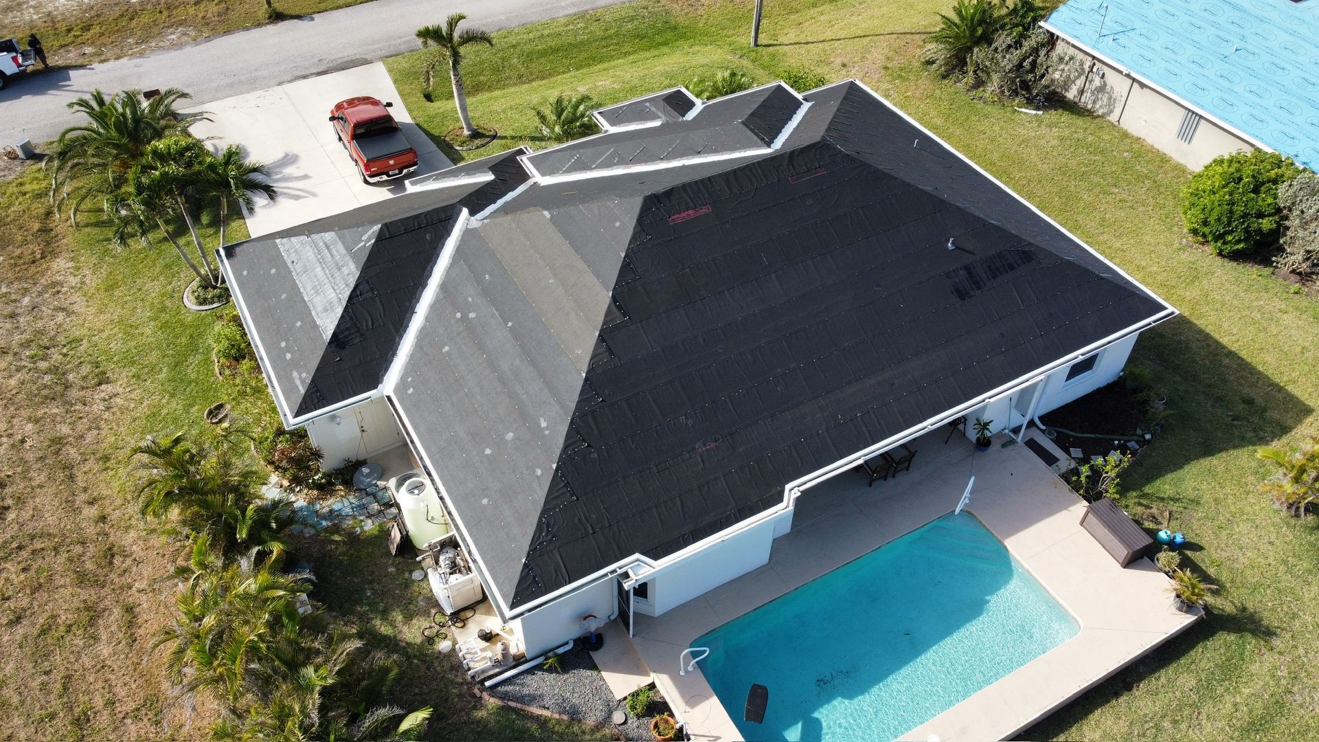 Aerial view of a white house with a dark roof, a pool, and a car parked in the driveway.