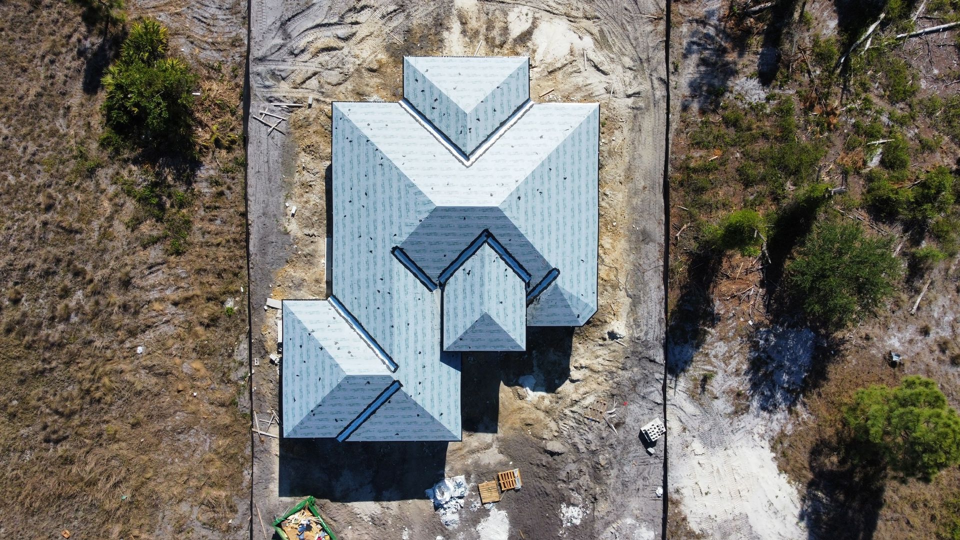 Aerial view of a house with a multi-gable roof. Construction site; gray and brown tones.