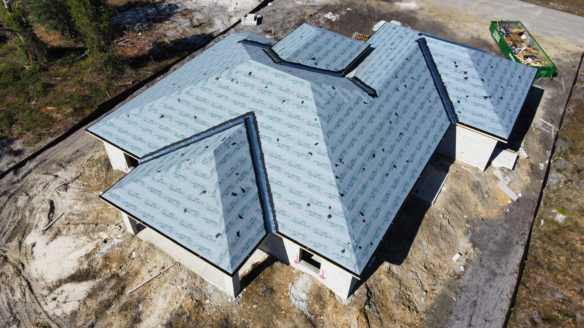 Aerial view of a house under construction with a partially completed blue-grey roof.