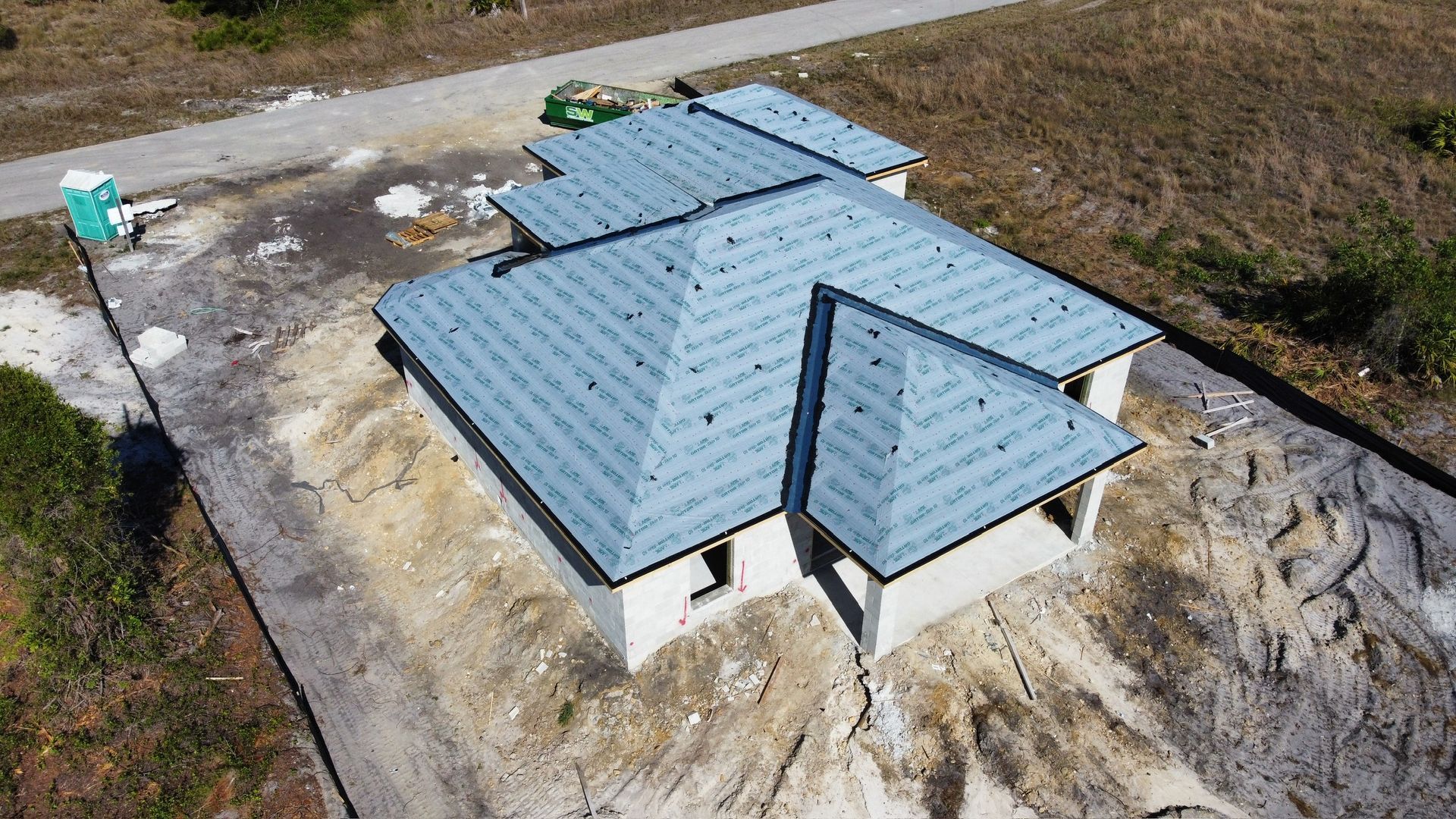 Aerial view of a house under construction with a gray roof on a dirt lot next to a road.