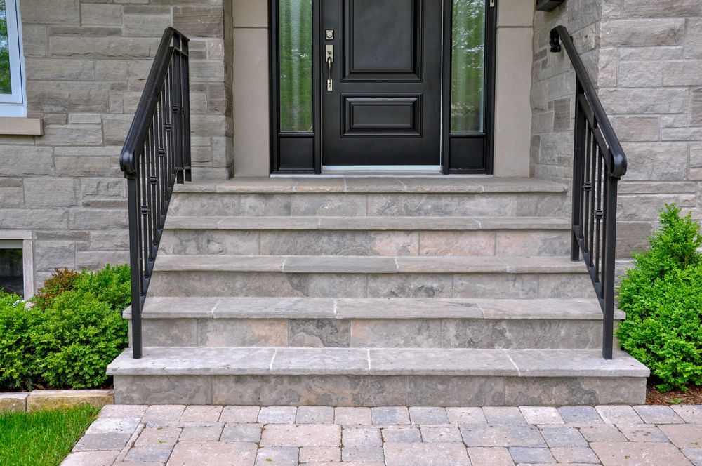 Stone steps leading to a black door with sidelights, flanked by black railings and greenery.