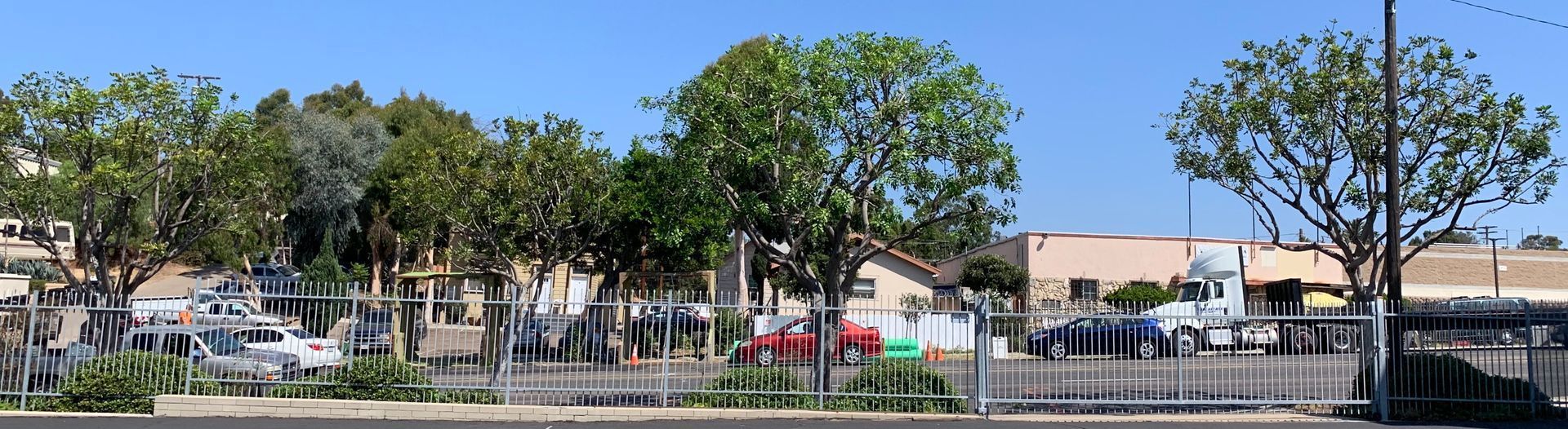 A fenced in area with trees and cars parked in front of a building.