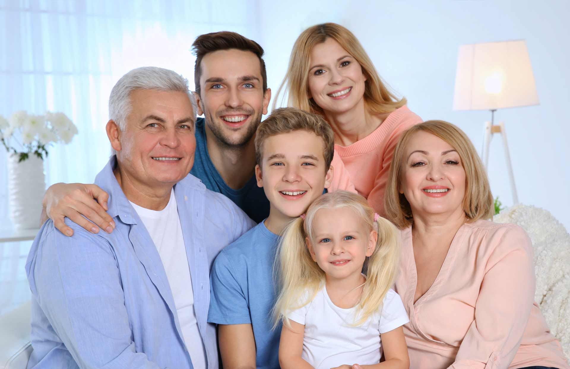 Smiling family seated together in a bright living room, with two adults, two children, and an older man.