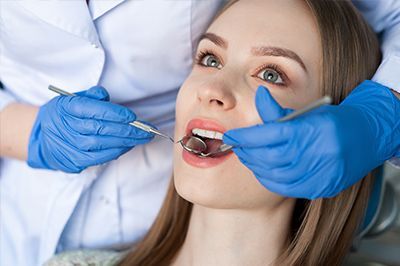 Dentist examining a patient’s open mouth with blue gloves and dental tools