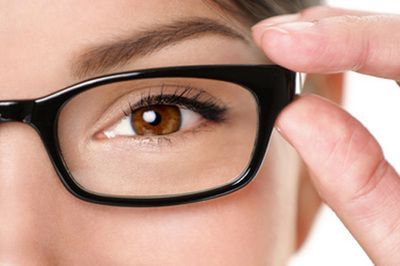 Close-up of an eye behind black eyeglass frames, with a hand adjusting the glasses