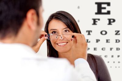 Optometrist adjusting eyeglasses on a smiling patient during an eye exam, with vision chart in the background