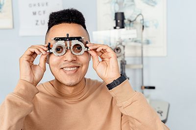 Smiling person holding a trial frame eyeglasses in a bright clinic setting