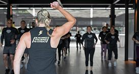 Woman leading a workout class, arm raised. People in black workout clothes exercise in a studio.