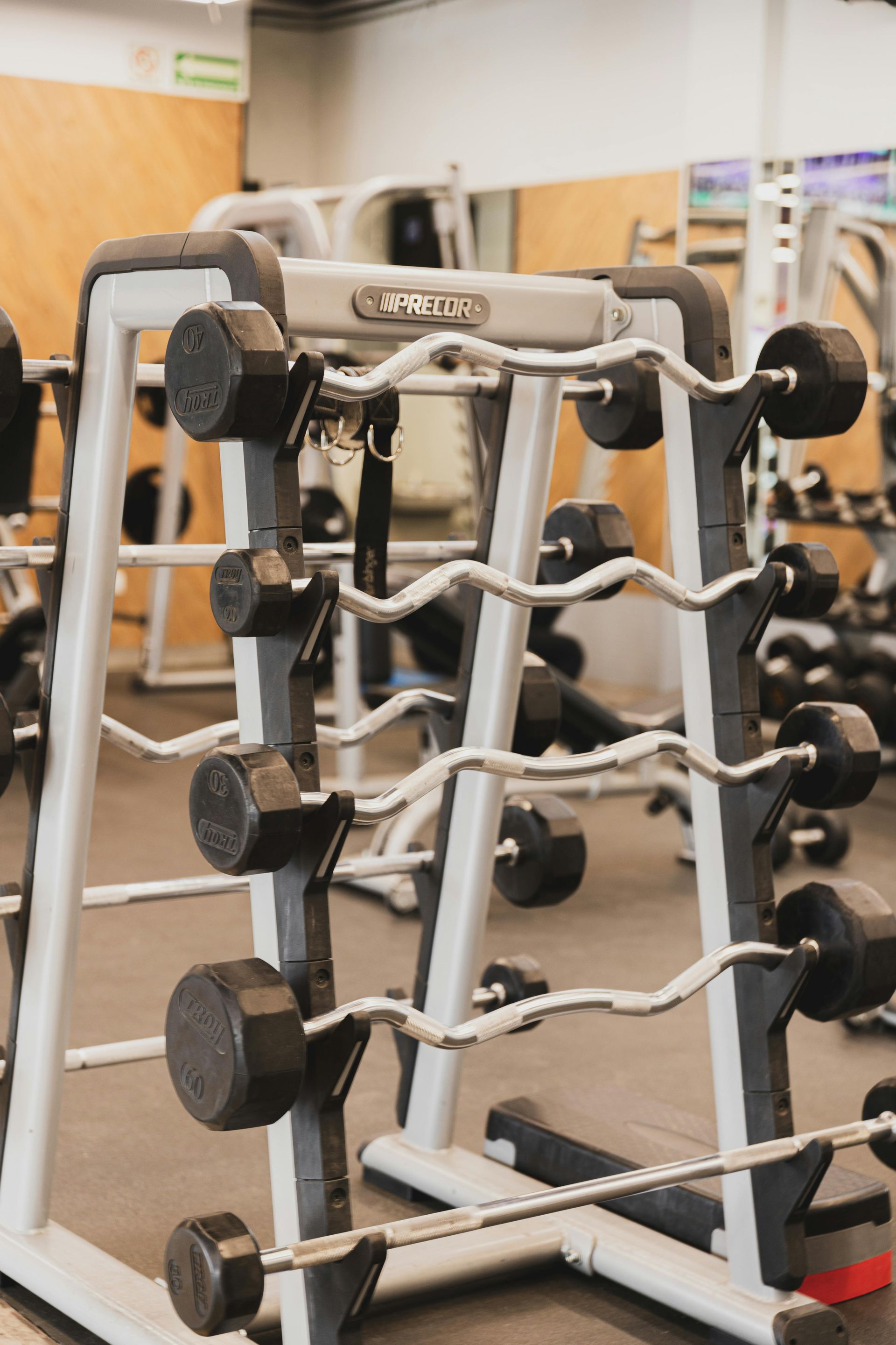 Rack of Precor EZ curl bars and dumbbells in a gym setting.