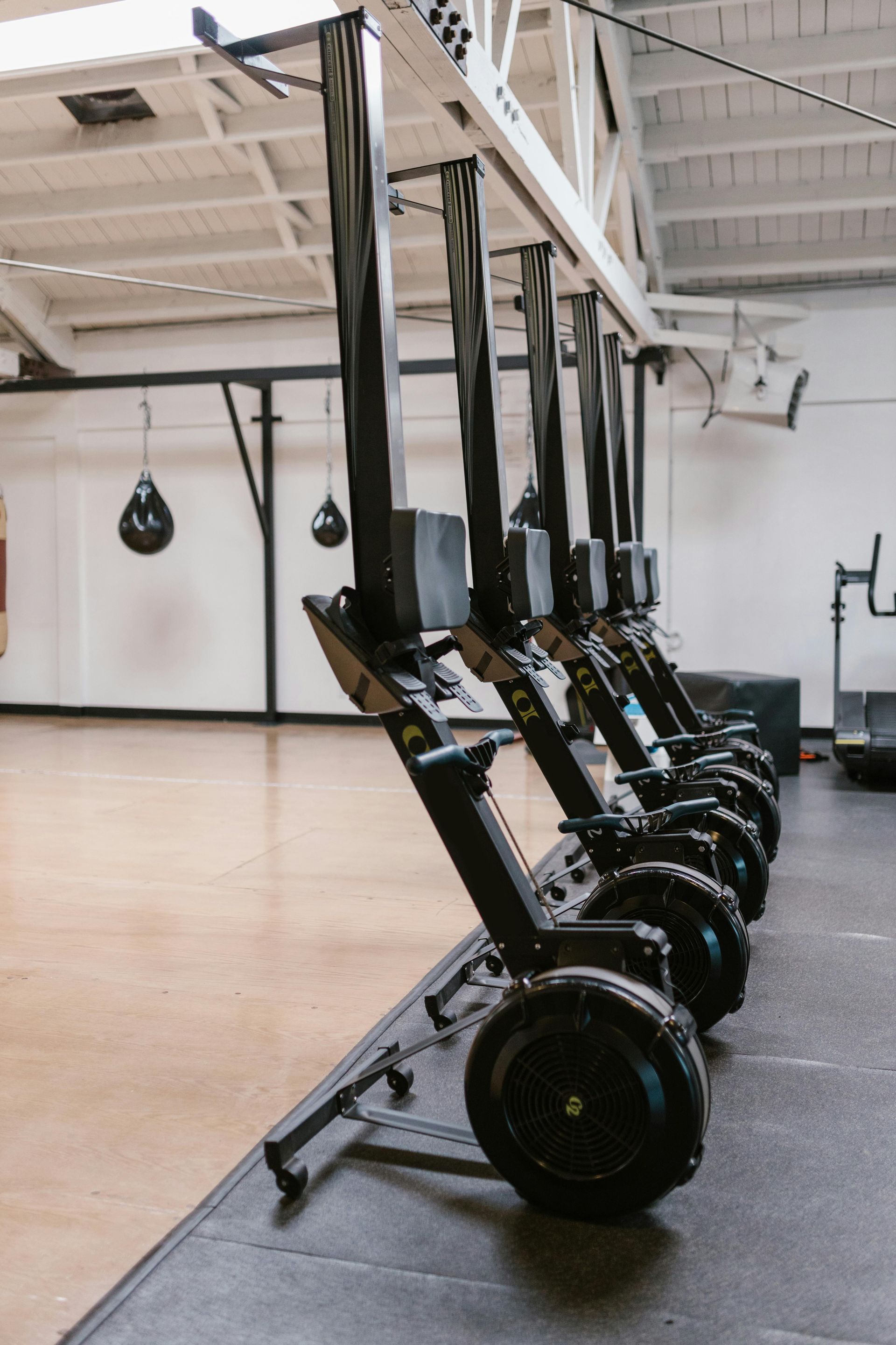 Rowing machines lined up in a gym, with a boxing bag in the background.