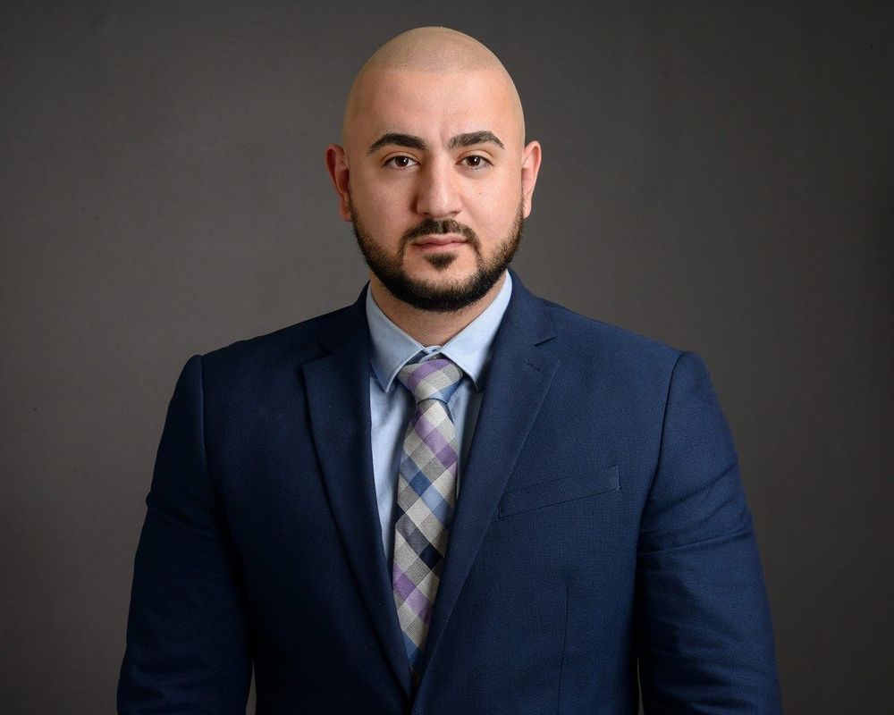 A man in a suit and tie is standing in front of a gray background.