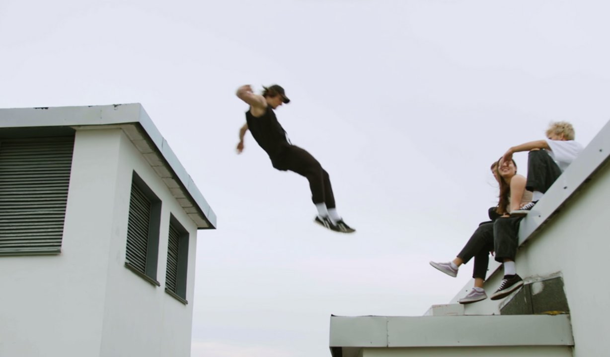 A man is jumping in the air while two people sit on the roof of a building.