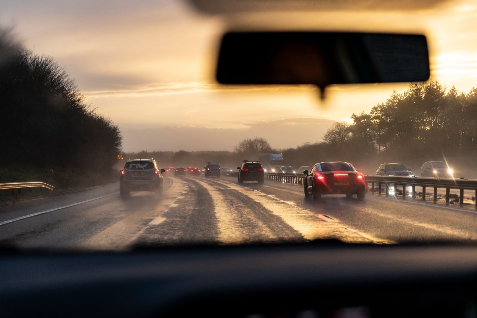 A car is driving down a wet highway at sunset.