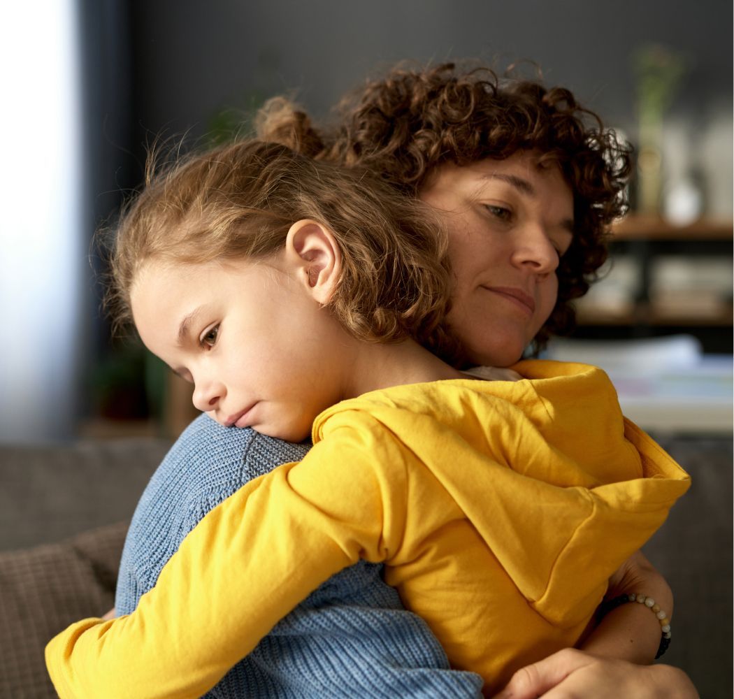 A woman is hugging a little girl on a couch.