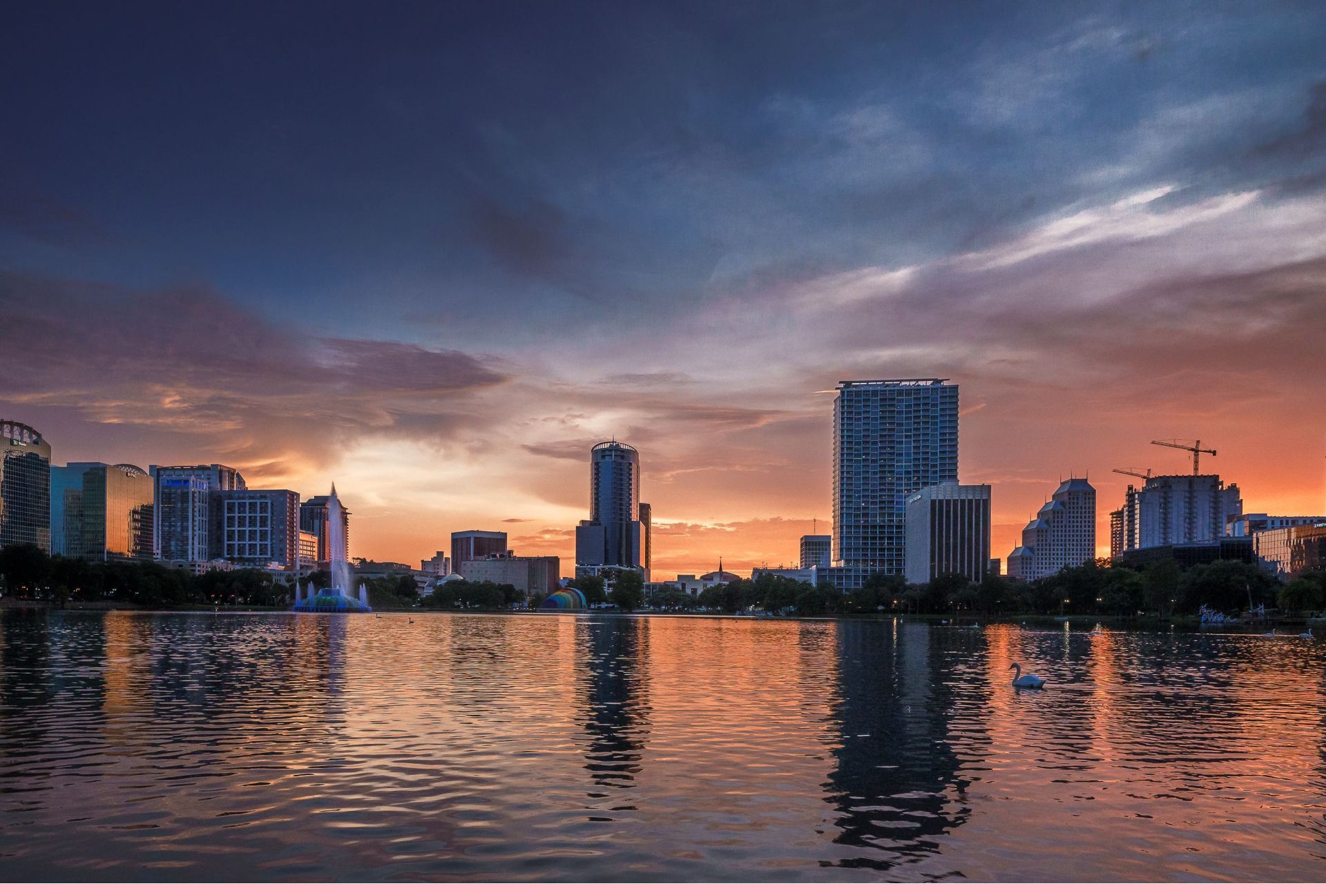 A city skyline is reflected in a lake at sunset.