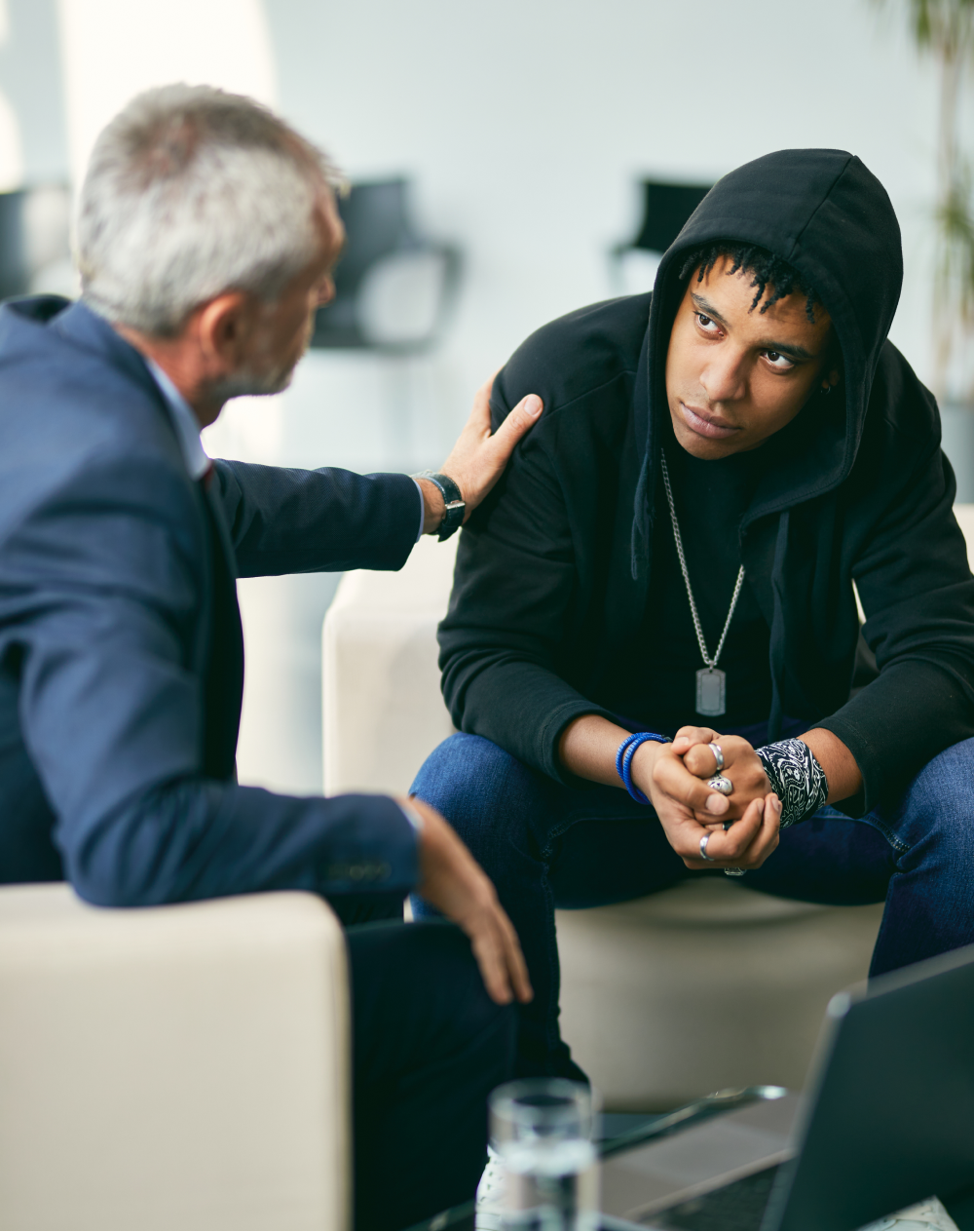 A man in a suit is comforting a young man in a black hoodie