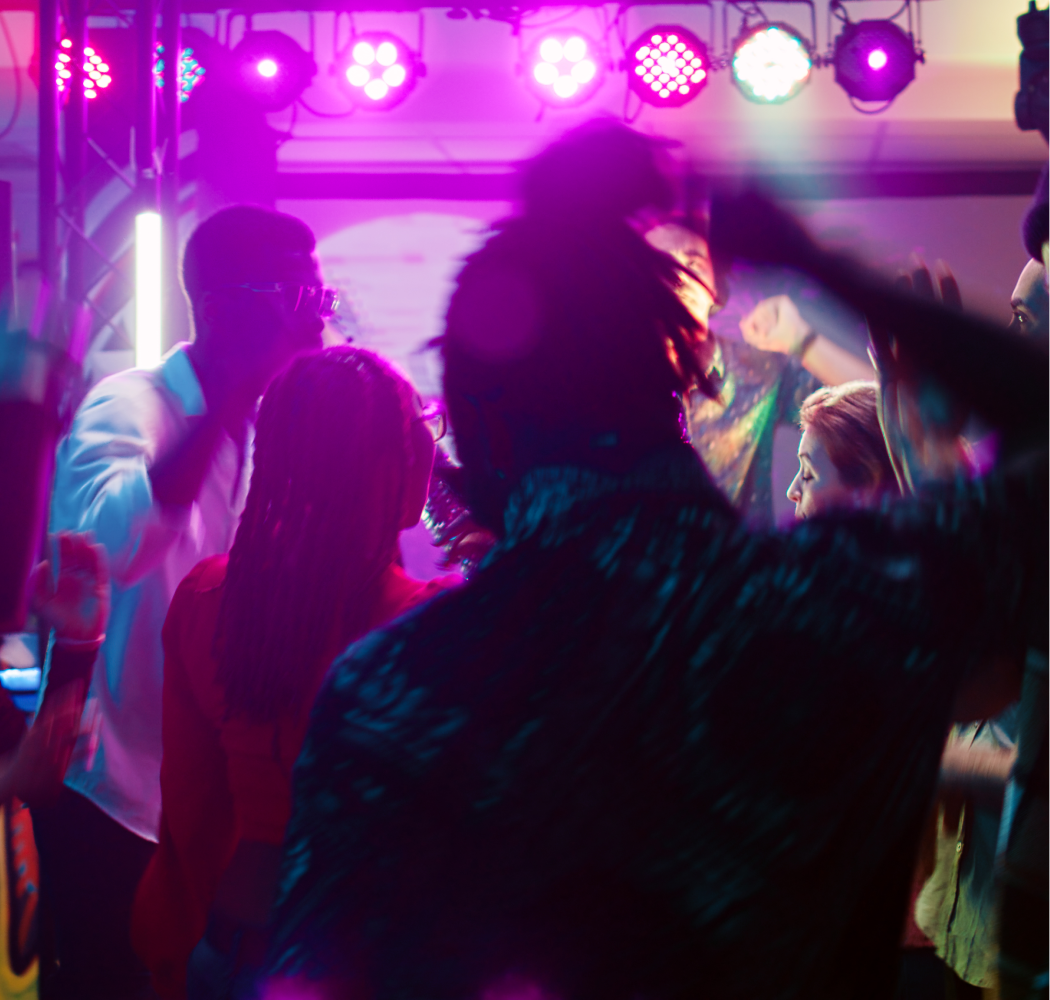 A group of people are dancing in a dark room under purple lights.