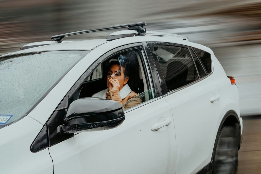 A woman is driving a white car and talking on a cell phone.