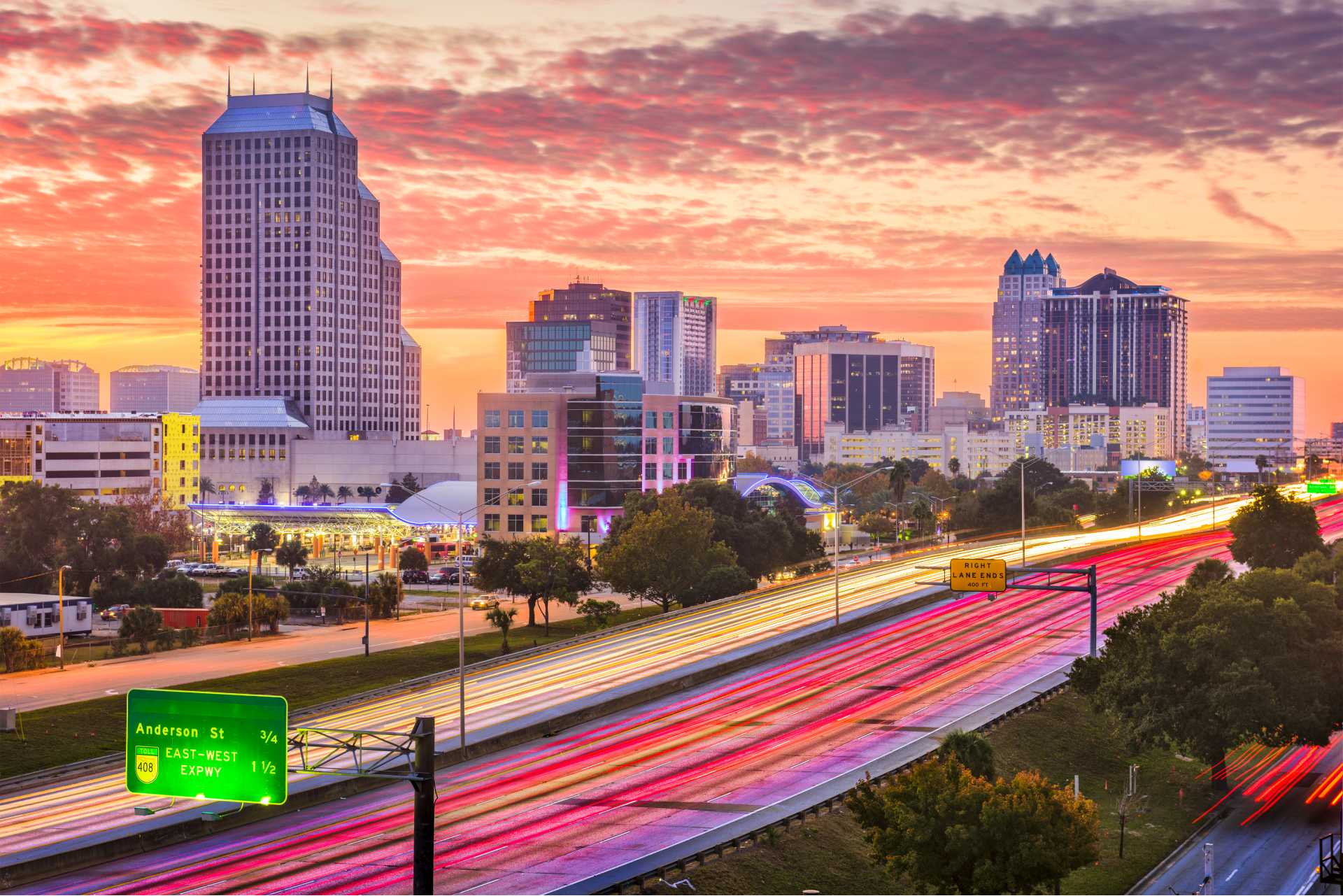 An aerial view of a city skyline at sunset with a highway in the foreground.