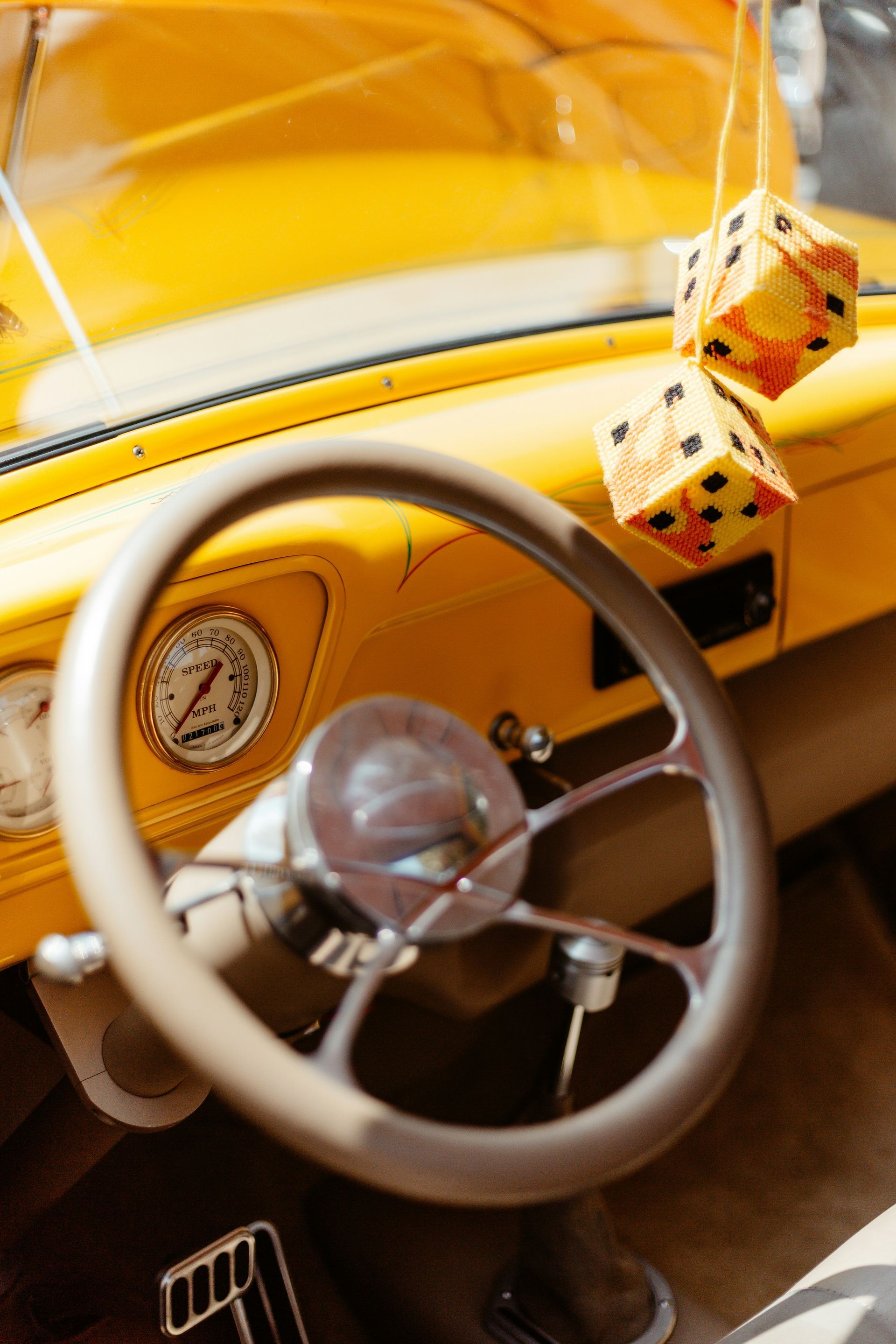 A yellow car with a steering wheel and dice hanging from the windshield