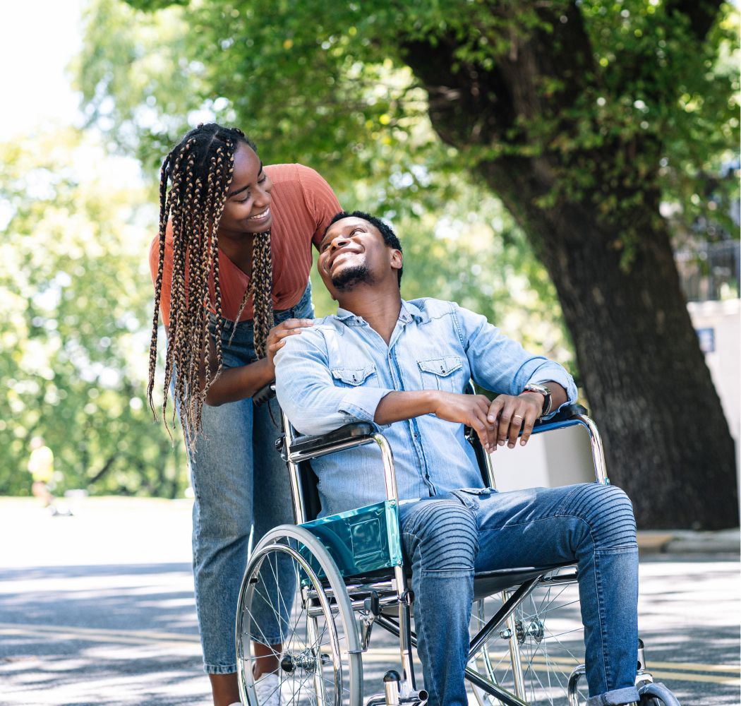 A woman is standing next to a man in a wheelchair.